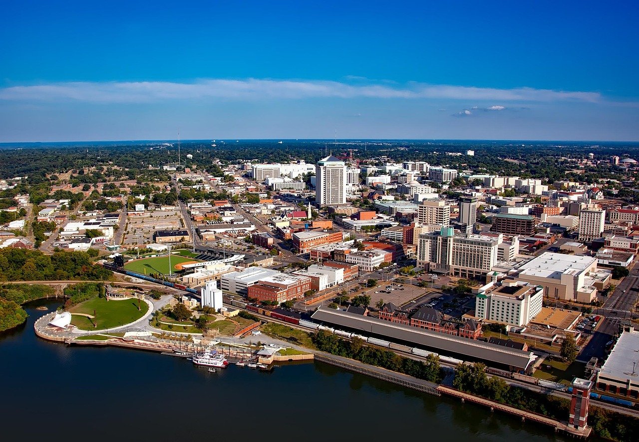 Alabama Towns : An aerial view of the Montgomery, Alabama skyline, showing the downtown area, the Alabama River, and Riverwalk Park on a sunny day.