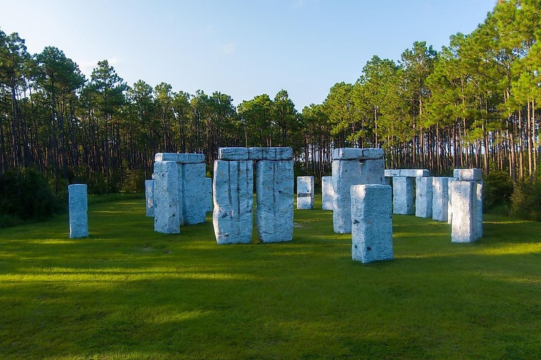 A full-scale fiberglass replica of Stonehenge, known as Bamahenge, standing in a grassy field backed by a pine forest in Alabama.