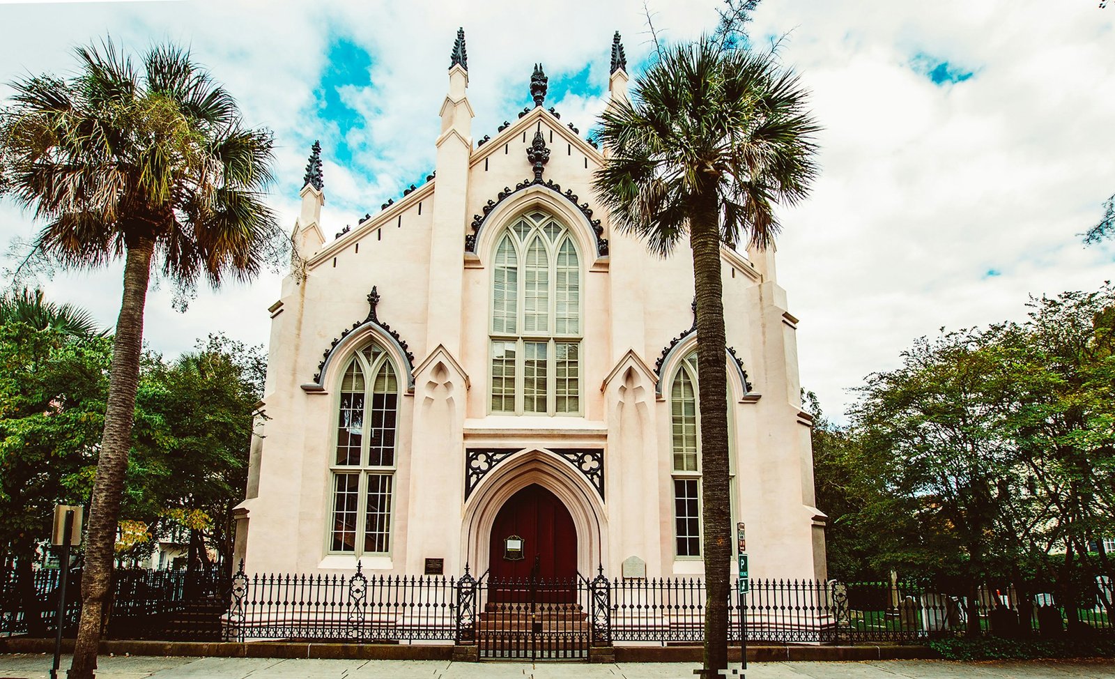 A historic light-colored church with Gothic architectural details and tall arched windows, framed by two prominent palm trees, in Charleston, South Carolina.