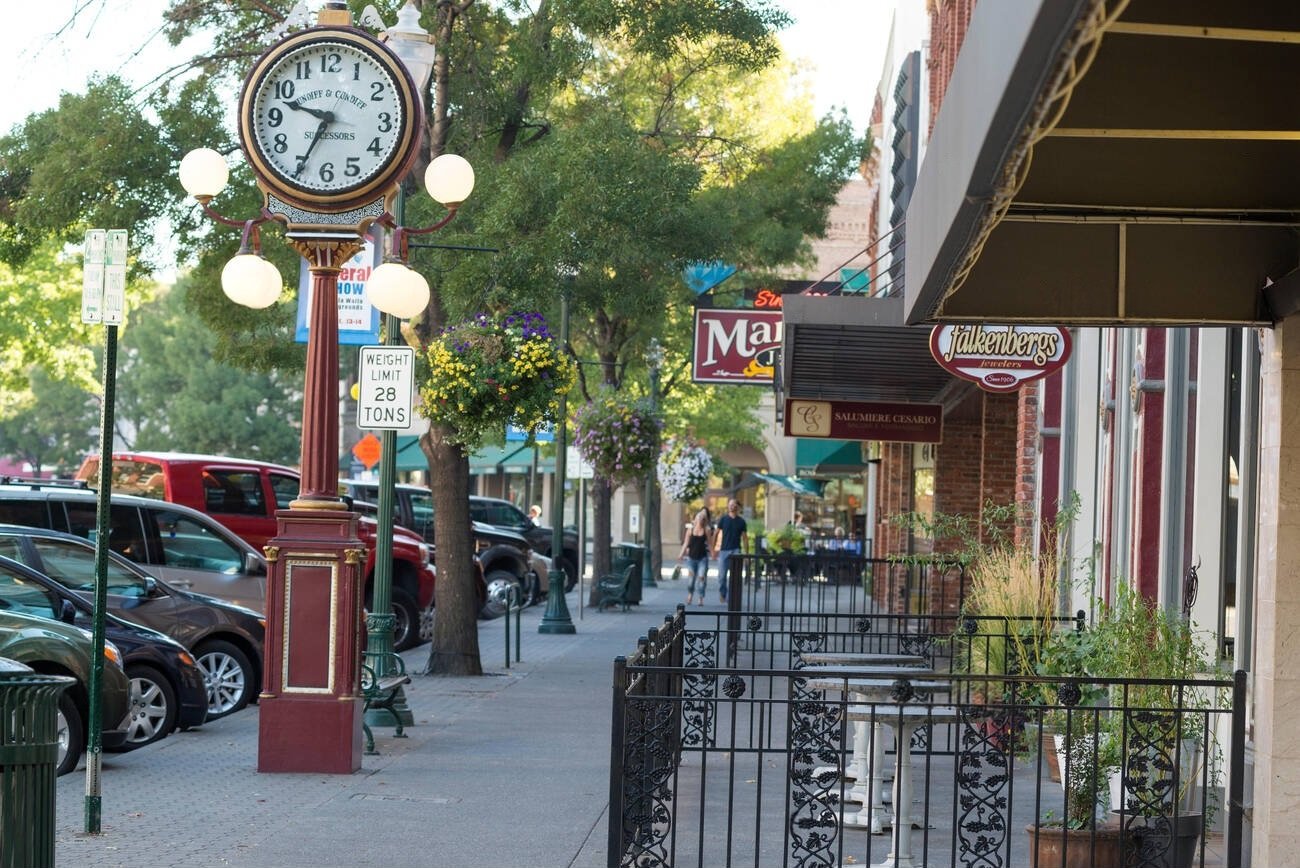 A charming downtown street in a small Washington town, featuring a vintage street clock, storefronts, and hanging flower baskets.