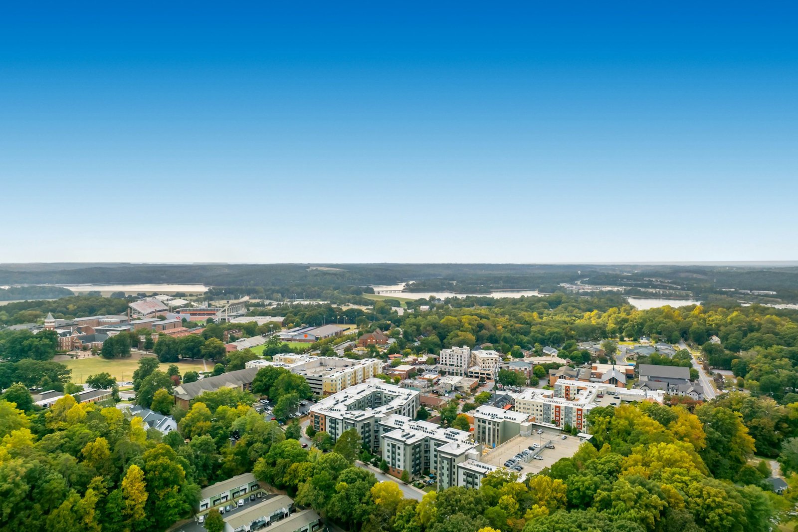 An aerial view of Clemson, South Carolina, showing the university campus, town buildings, and surrounding green foothills under a clear blue sky.