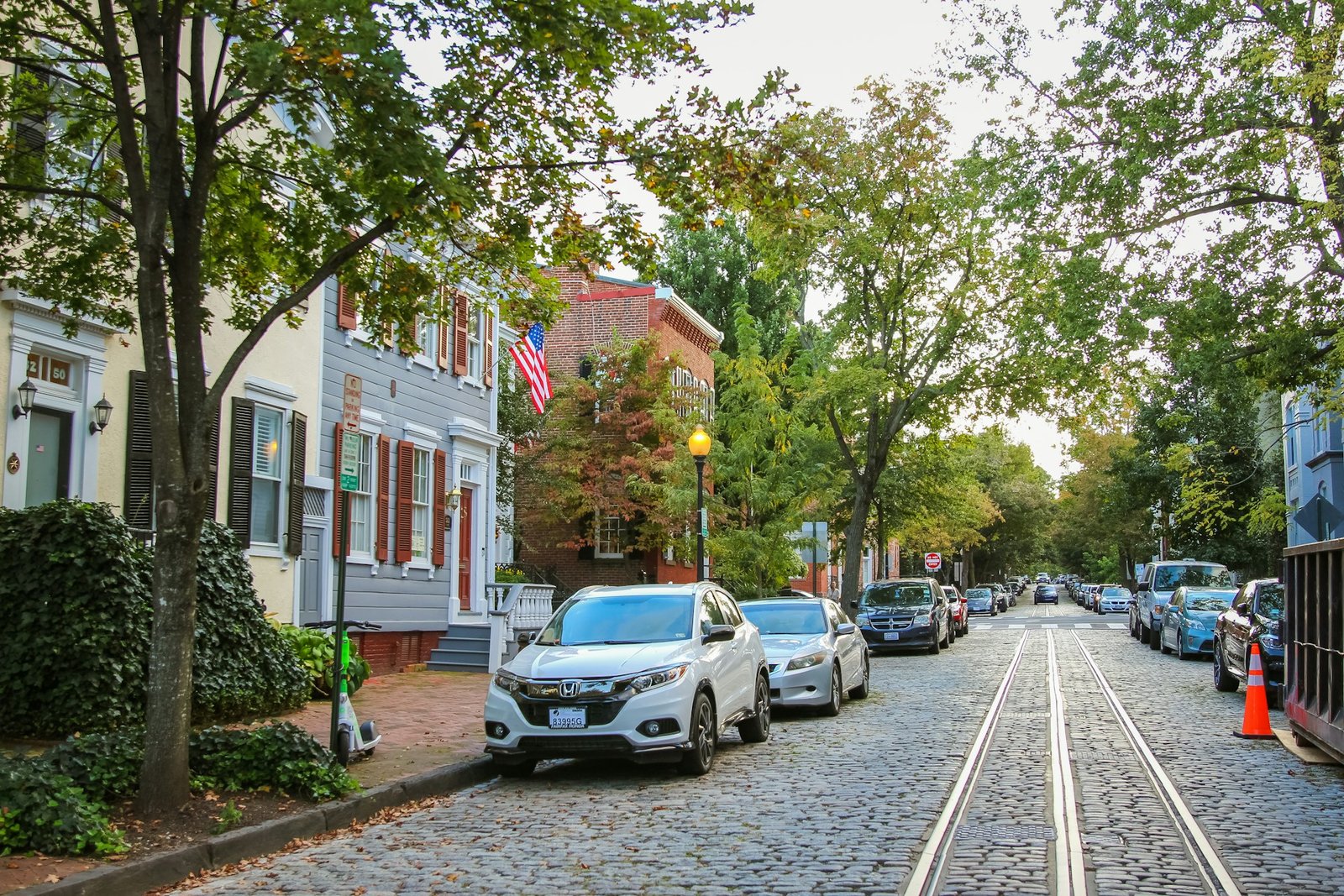 A historic cobblestone street with tram tracks and parked cars, lined by colorful buildings and trees, in Georgetown, South Carolina.