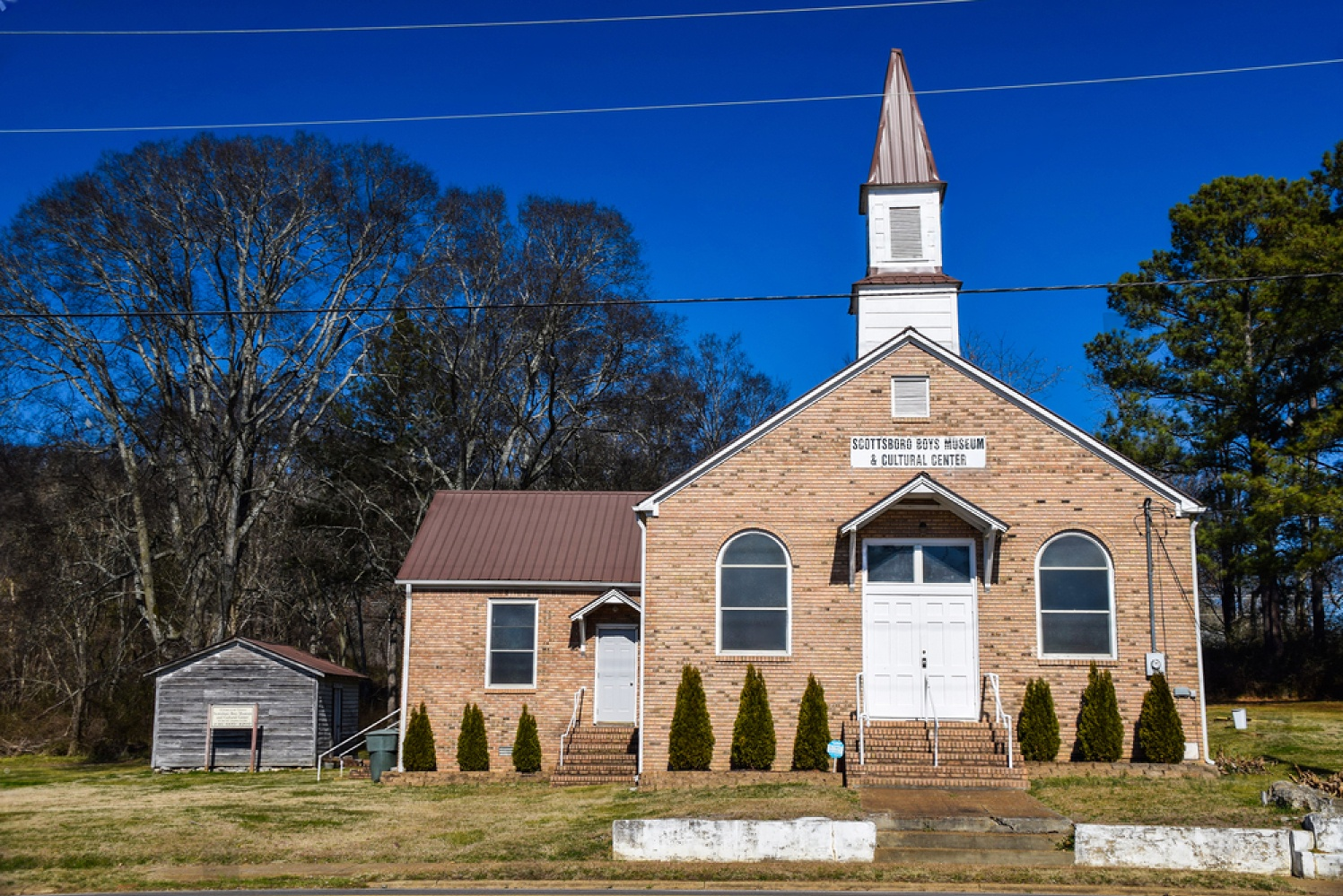 The Scottsboro Boys Museum and Cultural Center, a historic brick church building with a steeple, against a clear blue sky in Scottsboro, Alabama.