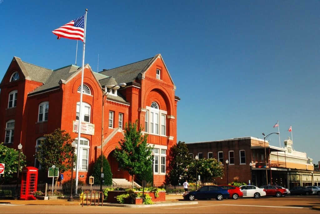 The historic red brick town hall on the square in Oxford, Mississippi, with an American flag and a red telephone booth in front.