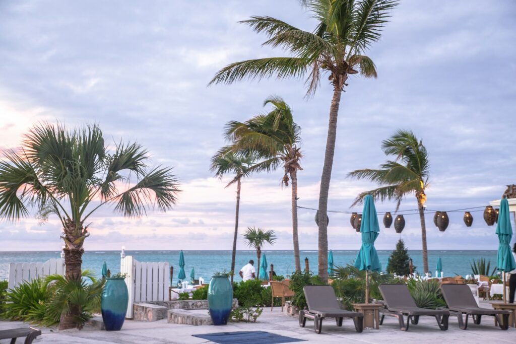A luxury beach resort patio on Grace Bay Beach at dusk, with palm trees, lounge chairs, and the turquoise ocean in the background.