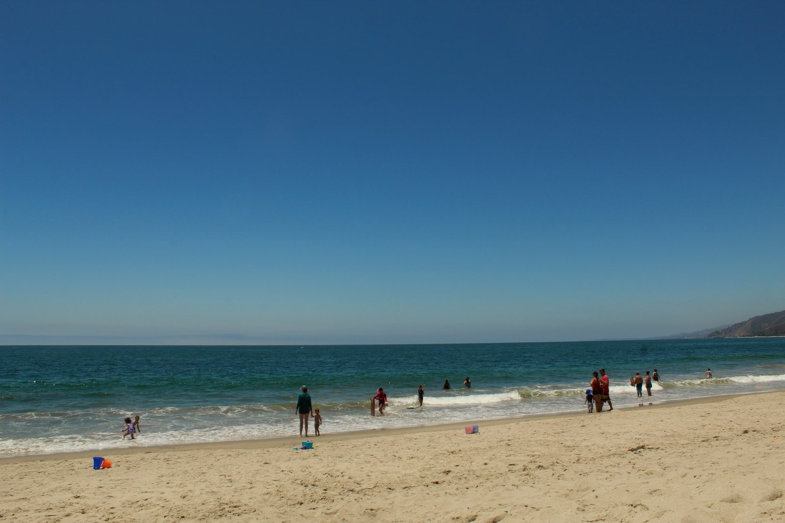 A wide sandy beach with people playing in the ocean under a clear blue sky, representing the coastal areas near McClellanville, South Carolina.