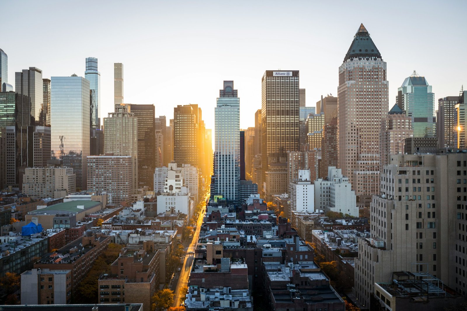 An aerial view of the New York City skyline at sunset, with sunlight reflecting off skyscrapers and illuminating a street below.