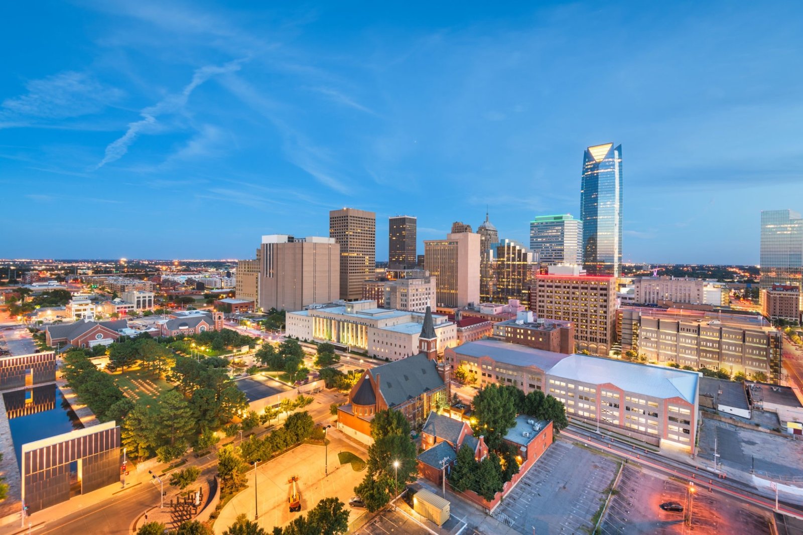 An aerial view of the Oklahoma City, Oklahoma downtown skyline at twilight, with city lights beginning to glow.
