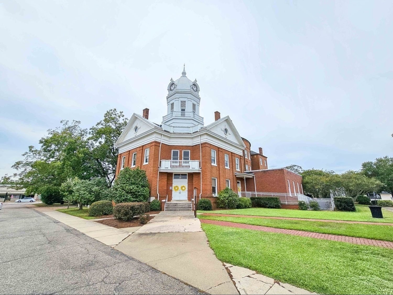 The historic Old Monroe County Courthouse in Monroeville, Alabama, a red brick building with a white clock tower, famous for its connection to "To Kill a Mockingbird."