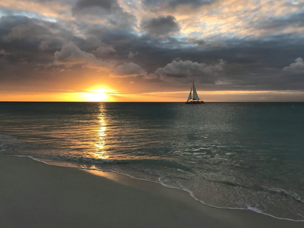 A sailboat on the ocean at Eagle Beach, Aruba, during a dramatic golden sunset.