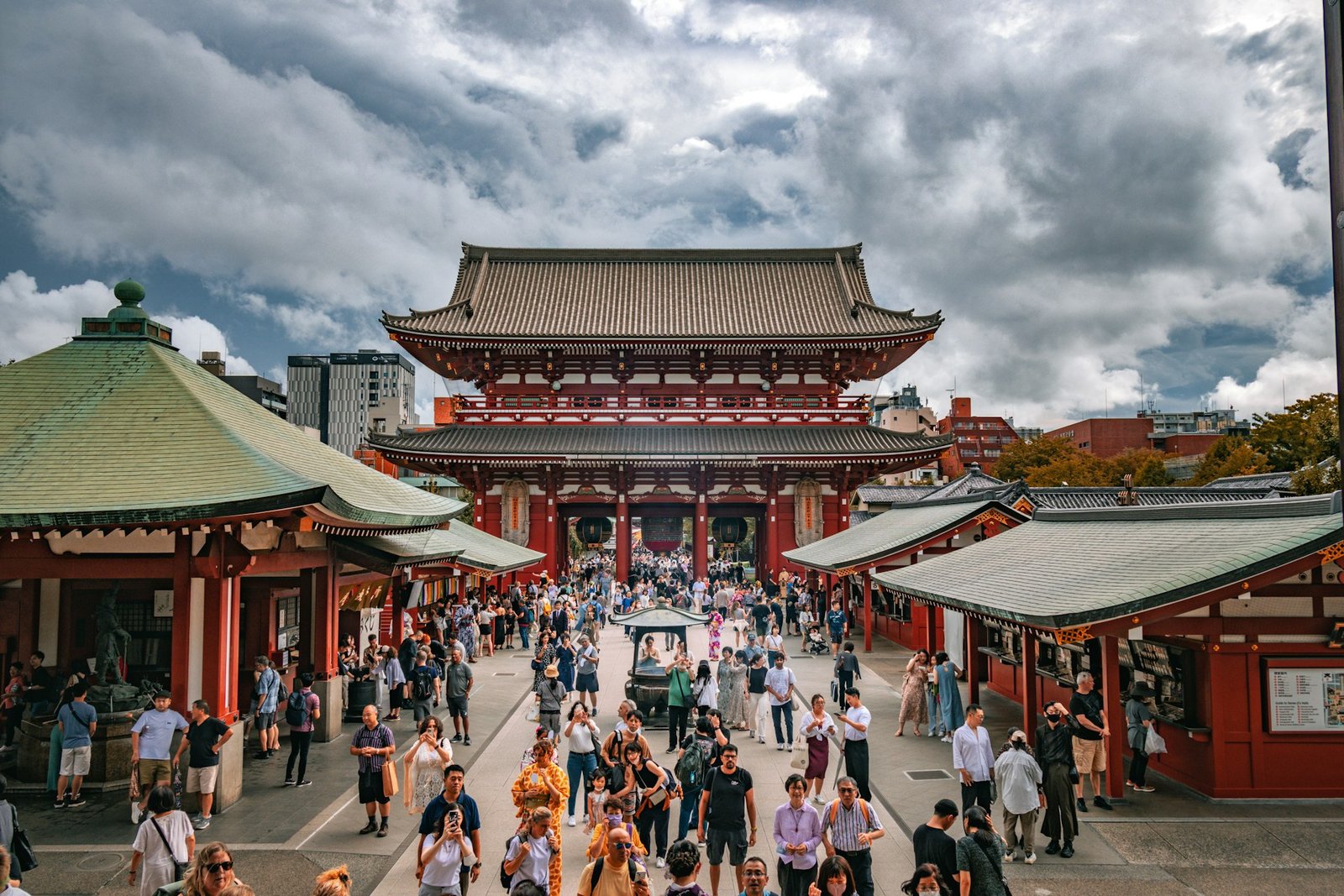 An elevated view of a large crowd of tourists at the historic Sensō-ji Temple in Asakusa, Tokyo, under a dramatic cloudy sky.