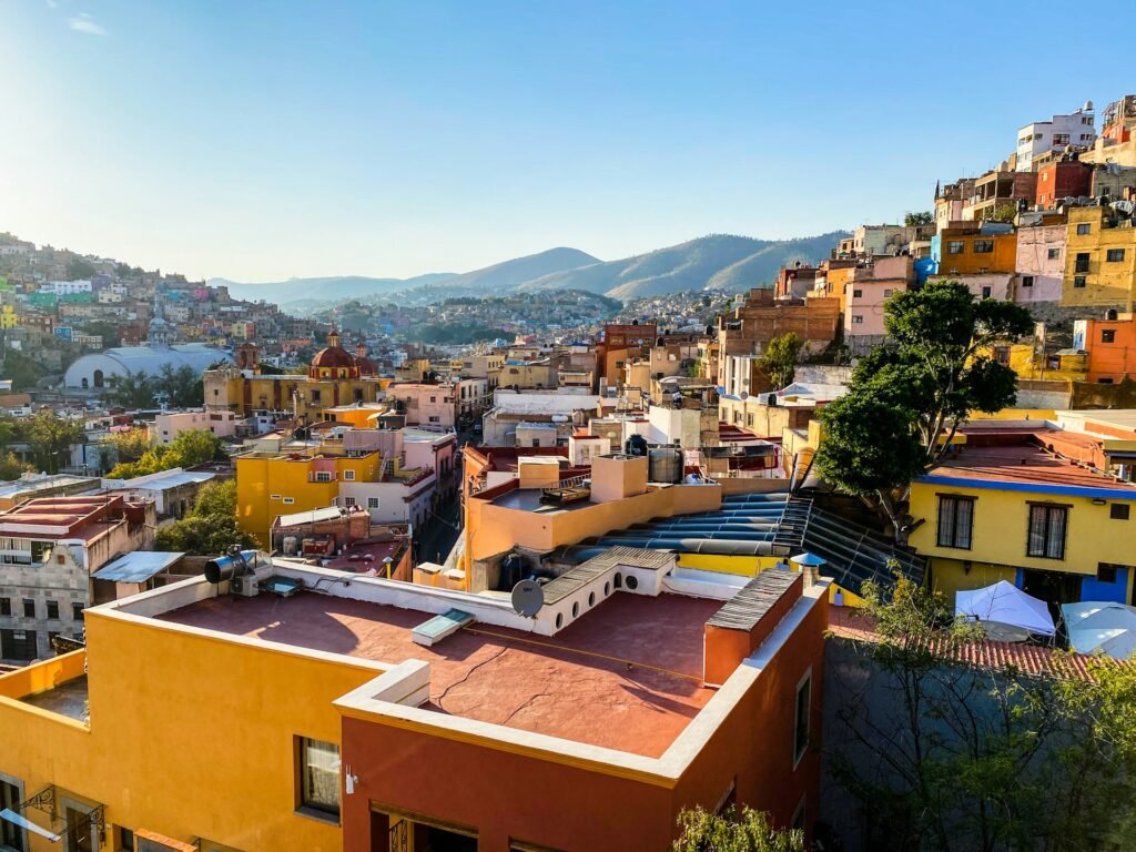 An elevated view of the colorful, hillside city of Guanajuato, Mexico, on a sunny day with mountains in the background.