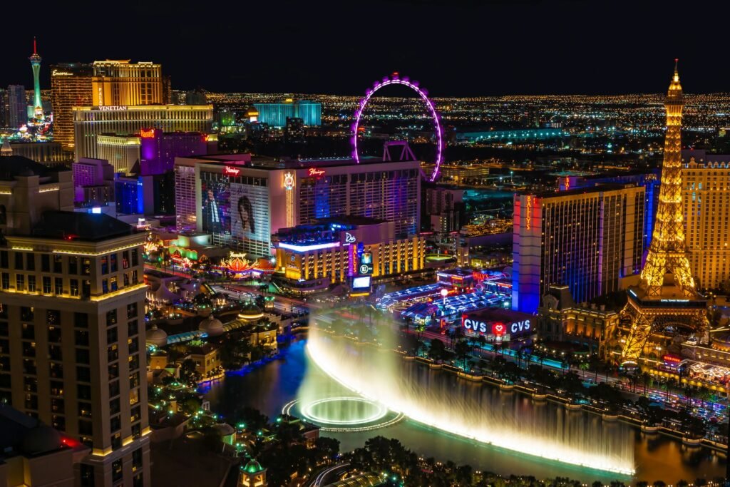 n aerial view of the Las Vegas Strip at night, showing the Bellagio fountains, the Paris hotel's Eiffel Tower, and the High Roller wheel.