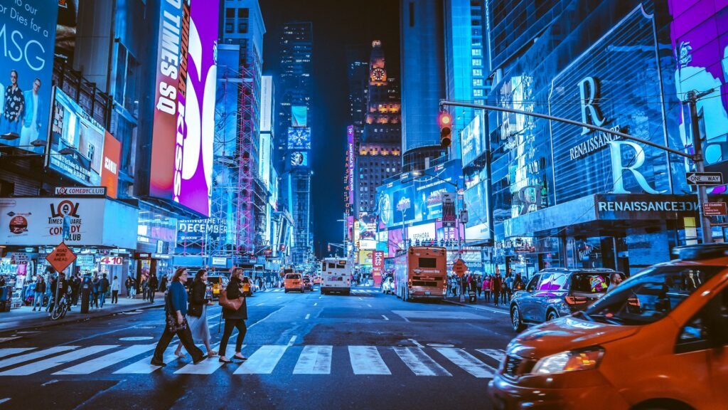 A vibrant night scene in Times Square, New York City, with people crossing the street under bright, colorful billboards.