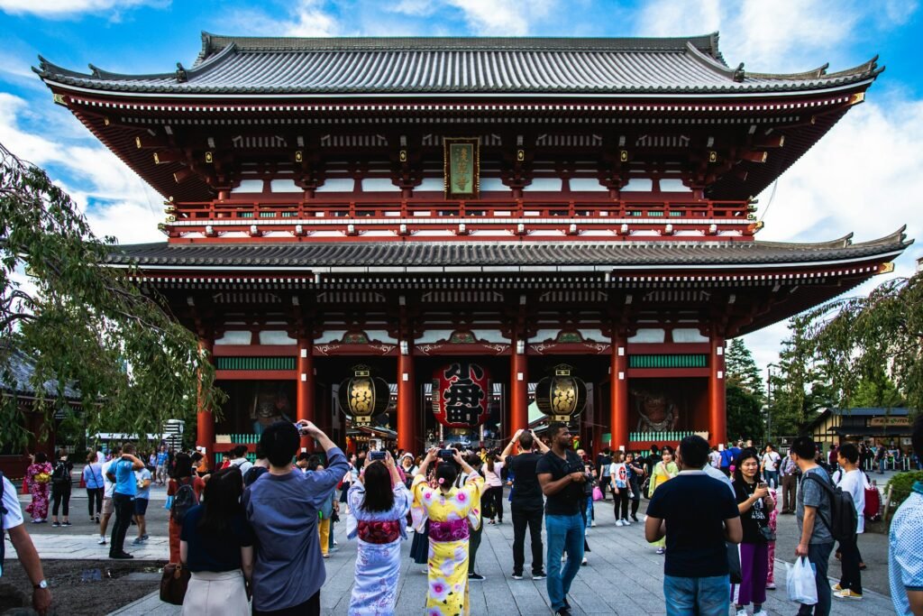 Tourists, including women in kimonos, taking photos of the large, red Hozomon Gate at Senso-ji Temple in Asakusa, Tokyo.