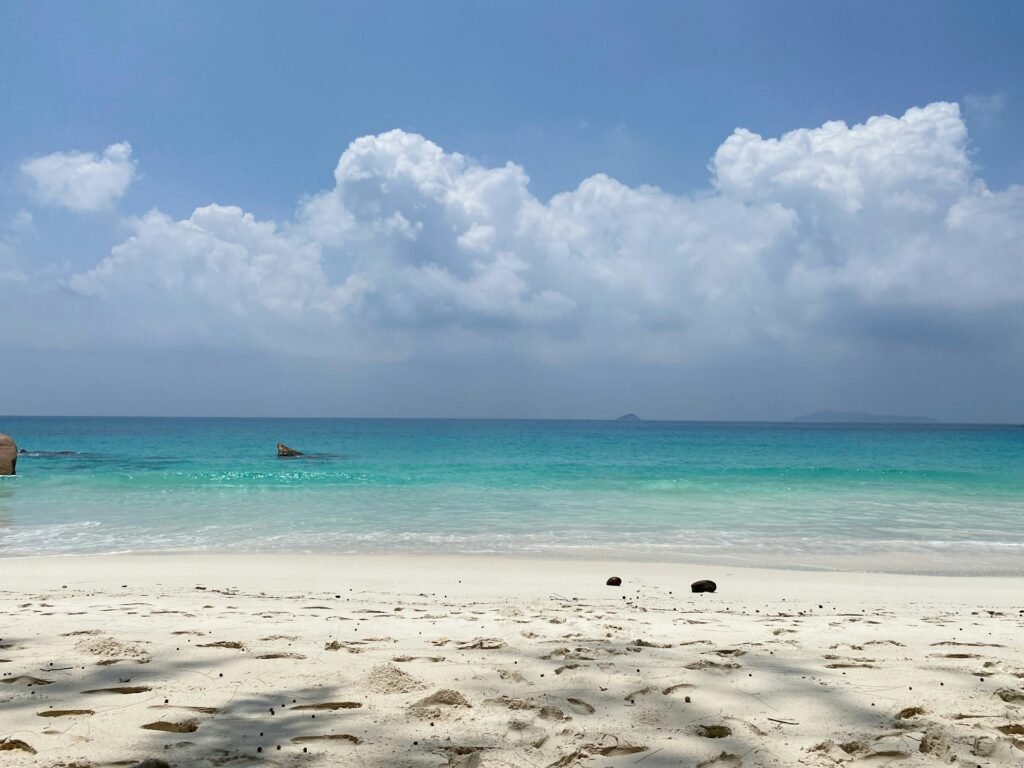 A serene view of the white sand and calm, turquoise water of Grand Anse Beach in Grenada on a partly cloudy day.