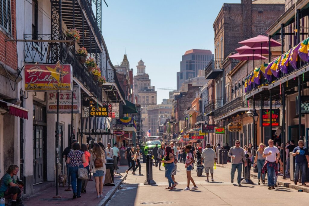 A busy street scene on Bourbon Street in the French Quarter of New Orleans, with people walking and historic buildings with iron balconies.