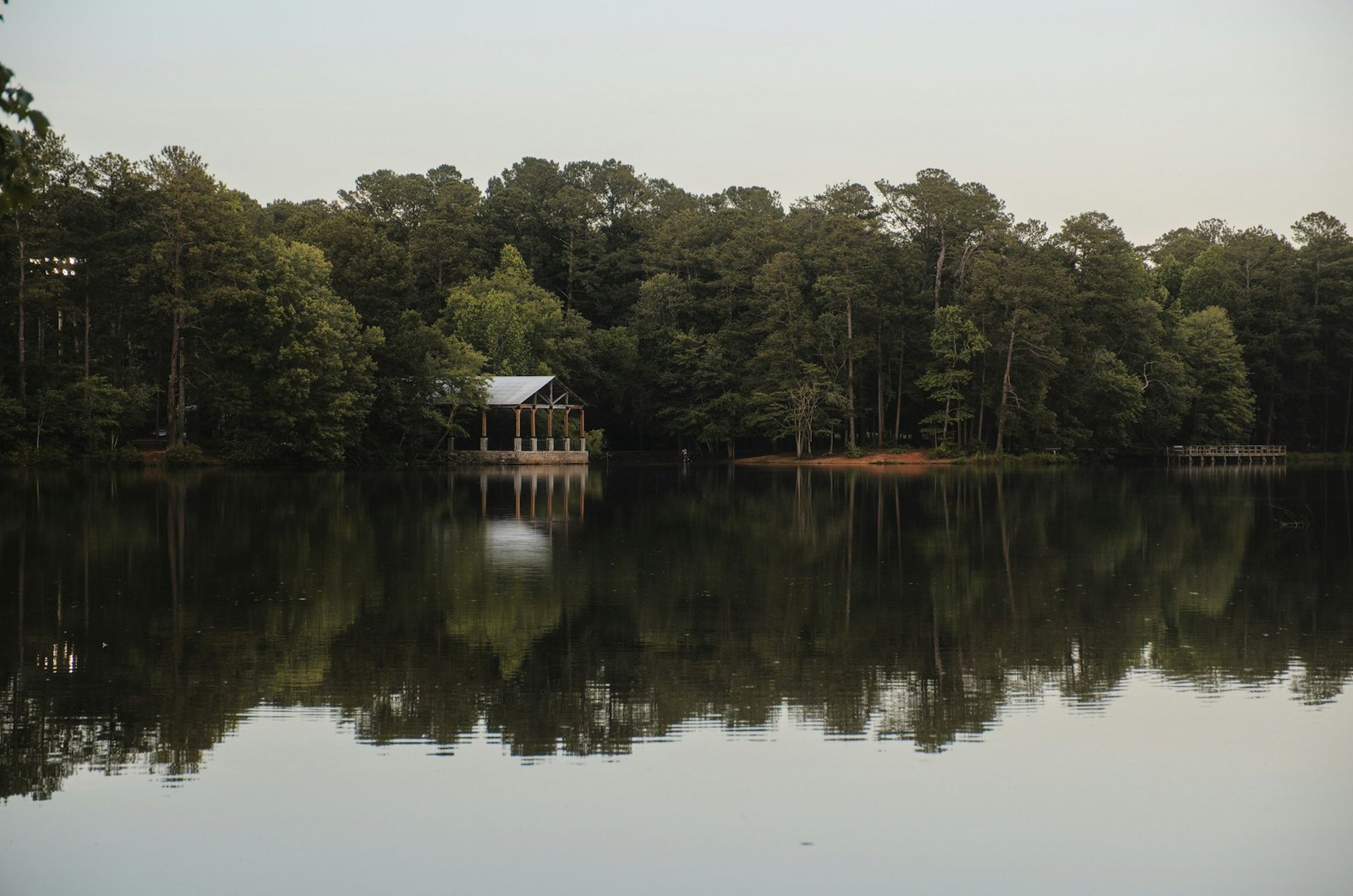 A serene lake with a wooden pavilion reflecting in the calm water, surrounded by dense green trees, typical of Walhalla, South Carolina's natural beauty.