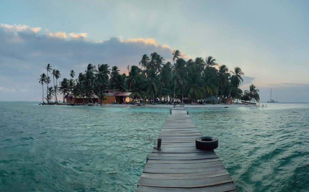 A wooden dock leading to a small, palm-tree-covered island in the San Blas archipelago, Panama, during a beautiful sunset.