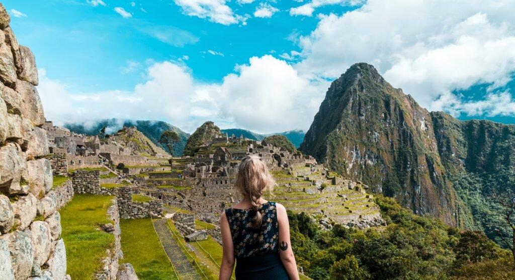 A woman looking out over the ancient Inca ruins of Machu Picchu in Peru, with the dramatic Andes mountains in the background.