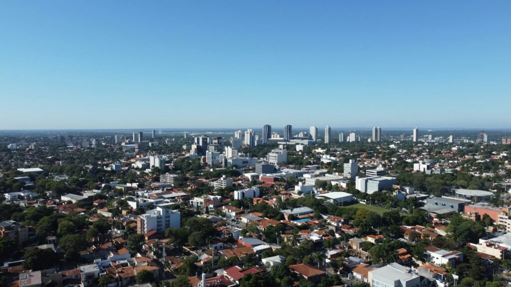 An aerial, panoramic view of the city of Asunción, Paraguay, showing a mix of low-rise neighborhoods and a modern downtown skyline.