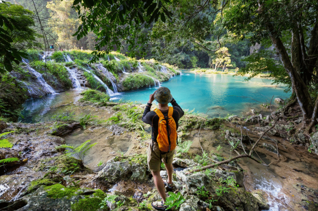 A traveler with a backpack looking out over the stunning turquoise pools and waterfalls of Semuc Champey in the Guatemalan jungle.