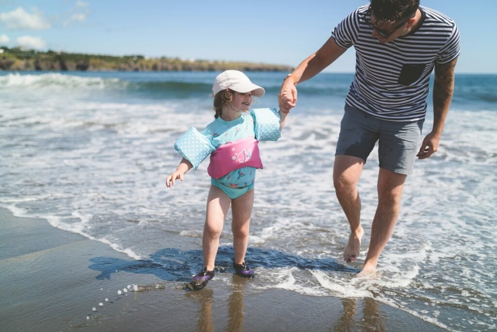 A father holding his young daughter's hand as they paddle in the gentle waves on a beach in Samoa.