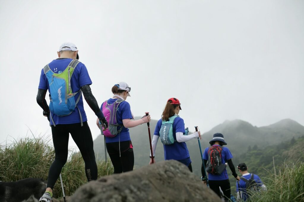 A group of hikers on the dark, ashy slope of Acatenango volcano in Guatemala, watching the nearby Fuego volcano erupt at night.