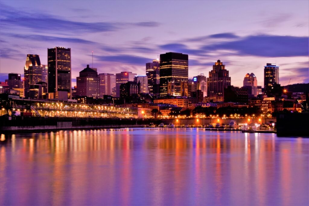 The Montreal city skyline illuminated at twilight, with the colorful lights of the city reflecting in the water of the Old Port.