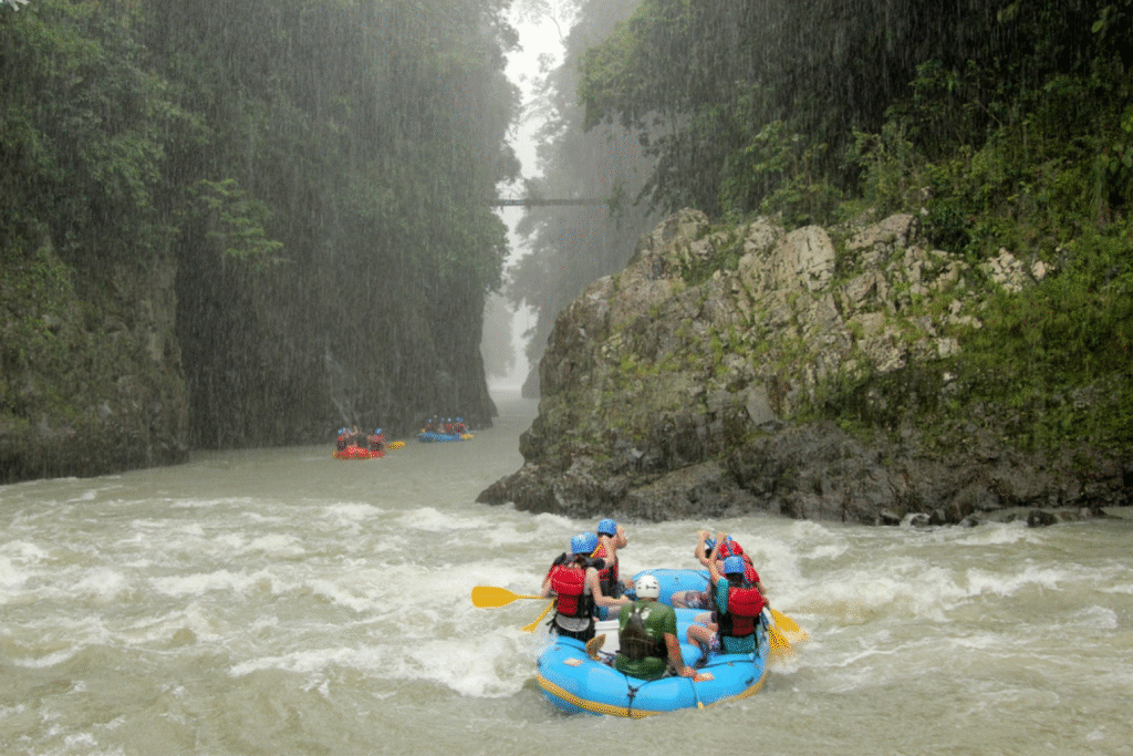 Central America Adventures:A team in a blue raft navigating the Pacuare River in Costa Rica during a rainstorm, with steep, jungle-covered canyon walls on either side.