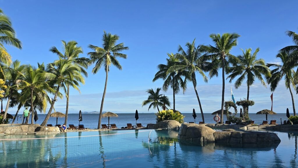 A hammock tied between two palm trees on a white sandy beach in Fiji, overlooking the calm, turquoise ocean.