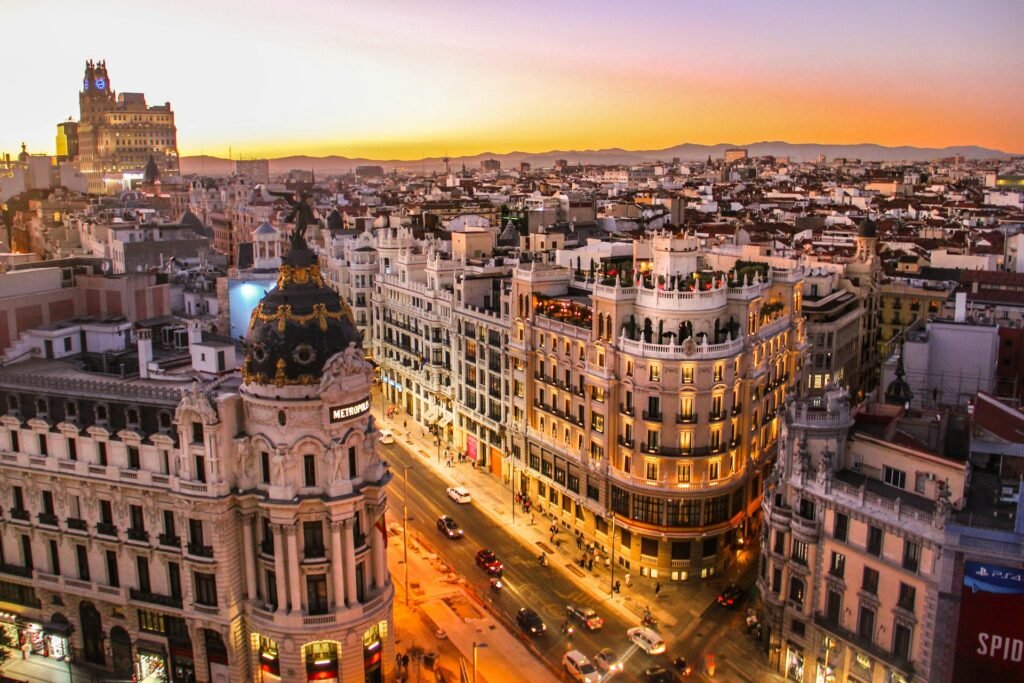 An aerial view of the Gran Vía in Madrid at sunset, featuring the iconic Metropolis Building and the city skyline.
