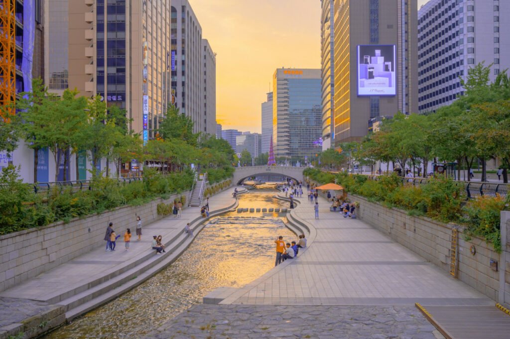People relaxing along the Cheonggyecheon Stream, a public recreation space in downtown Seoul, South Korea, at sunset.