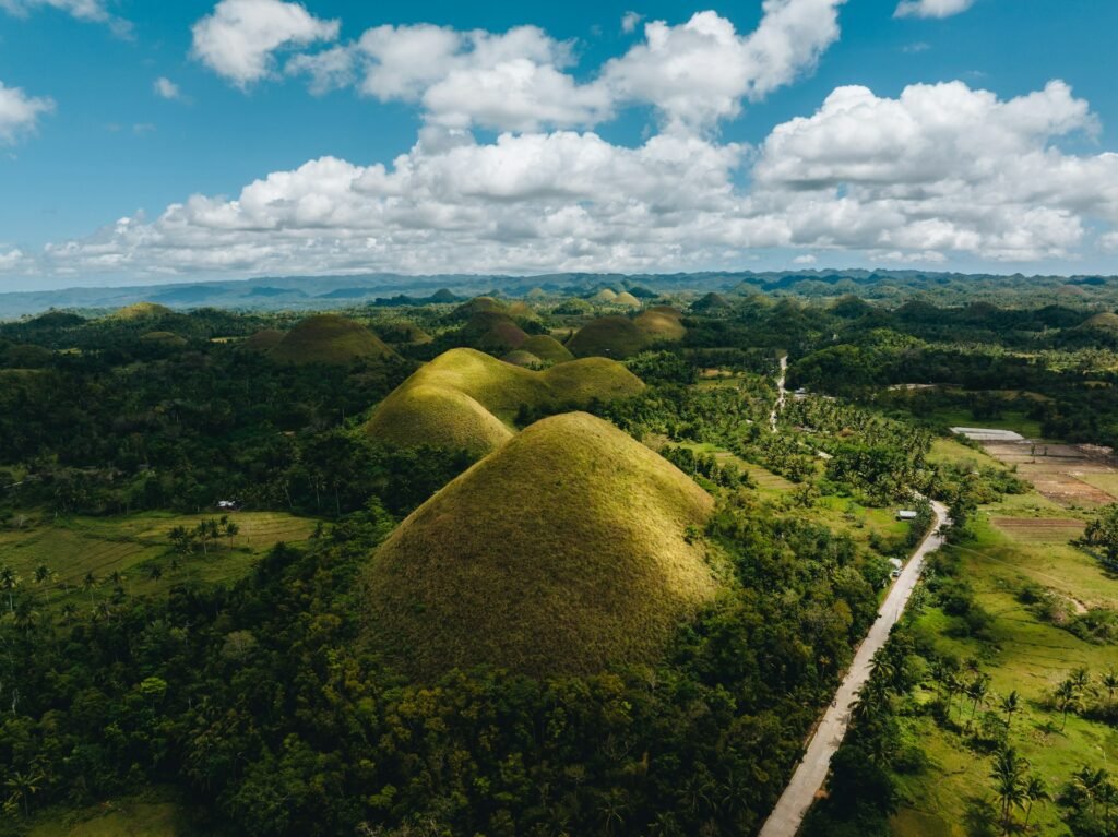 An aerial view of the famous Chocolate Hills in Bohol, Philippines, showing the unique, cone-shaped hills covered in green grass.