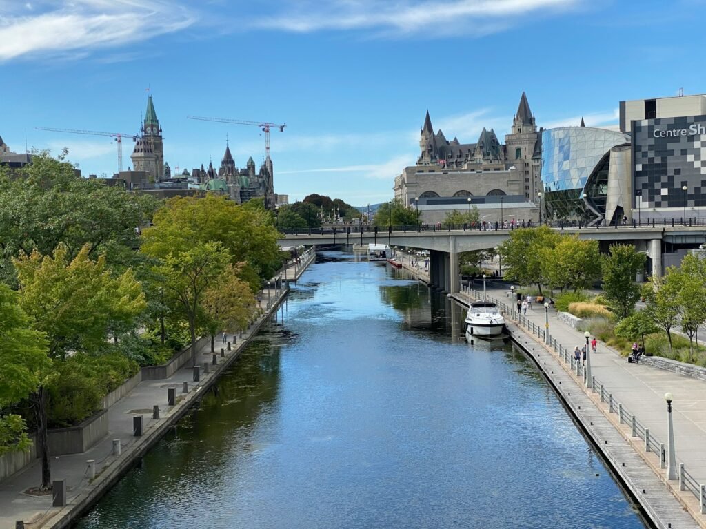 A view of the Rideau Canal in Ottawa on a sunny day, with the Parliament Buildings and the Château Laurier in the background.