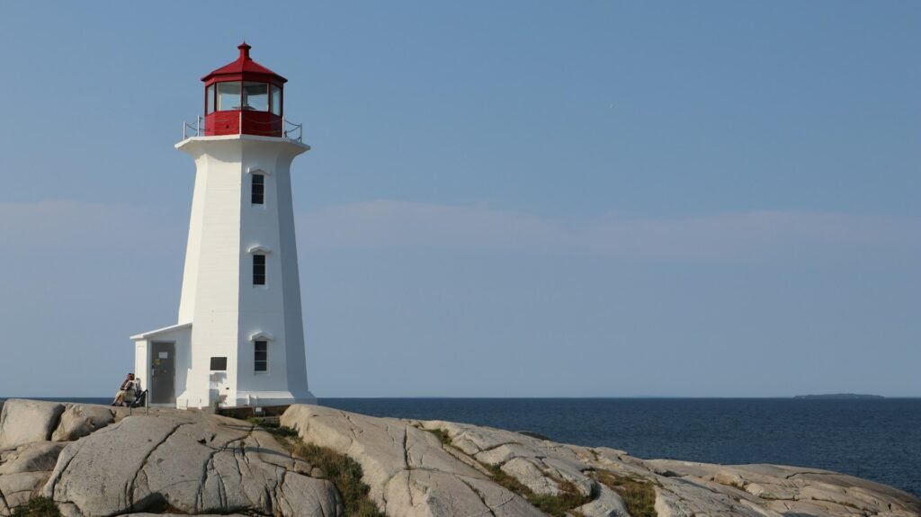 The iconic white and red lighthouse at Peggy's Cove, Nova Scotia, standing on a large granite outcrop overlooking the Atlantic Ocean.