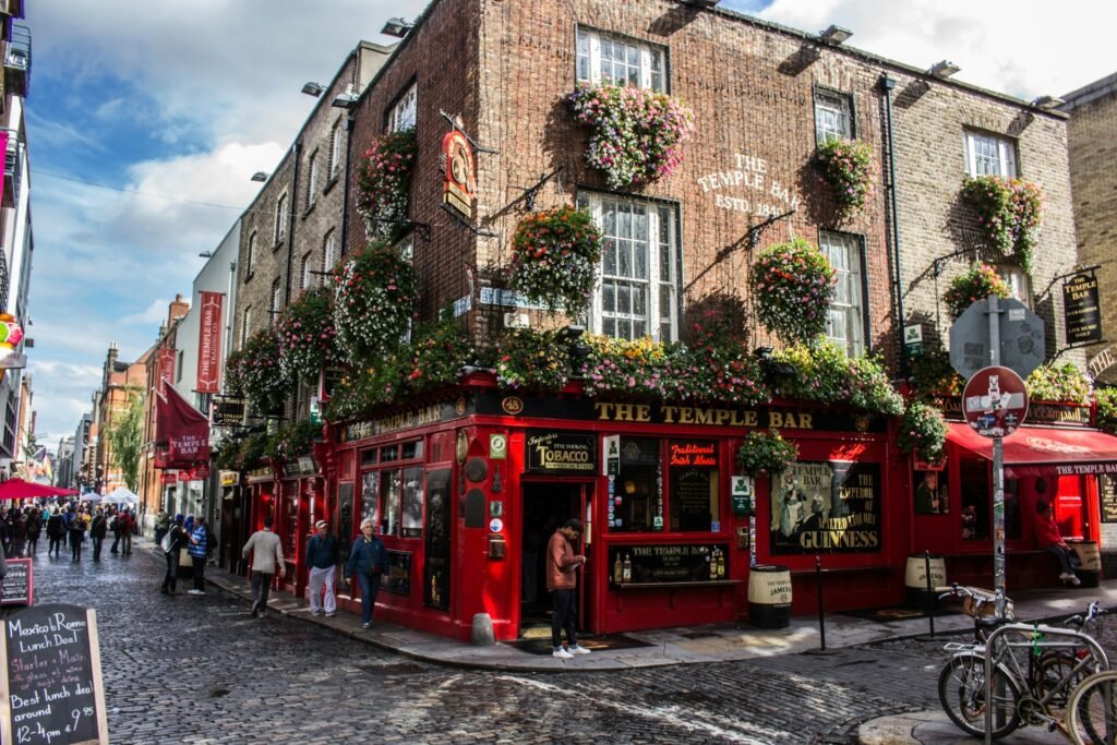 The famous red facade of The Temple Bar pub on a cobblestone street corner in Dublin, Ireland, decorated with hanging flower baskets.