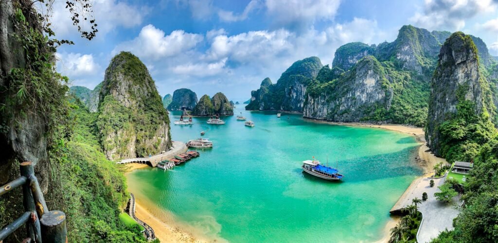 A panoramic, elevated view of tour boats on the emerald waters of Halong Bay, Vietnam, surrounded by towering limestone karsts.