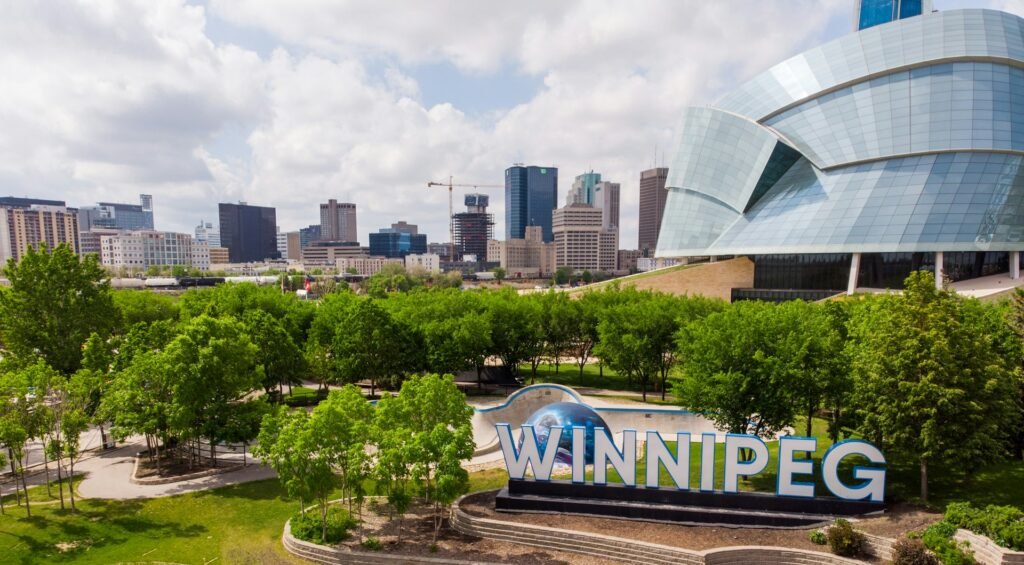 An aerial view of Winnipeg, featuring the iconic "WINNIPEG" sign, the Canadian Museum for Human Rights, and the downtown skyline.