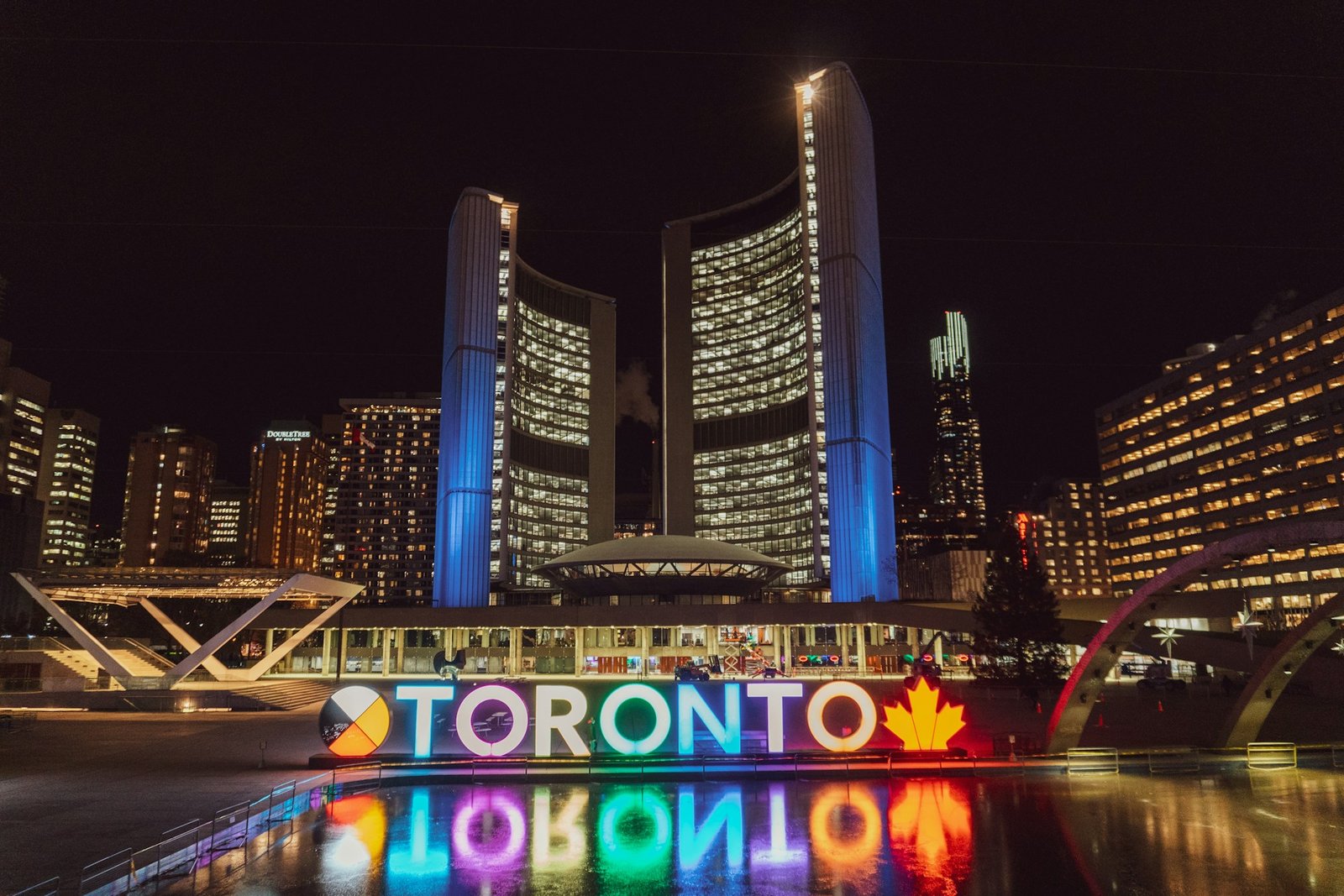 Canadian Cities : The illuminated Toronto City Hall and the colorful "TORONTO" sign at night, reflected in the water of Nathan Phillips Square.