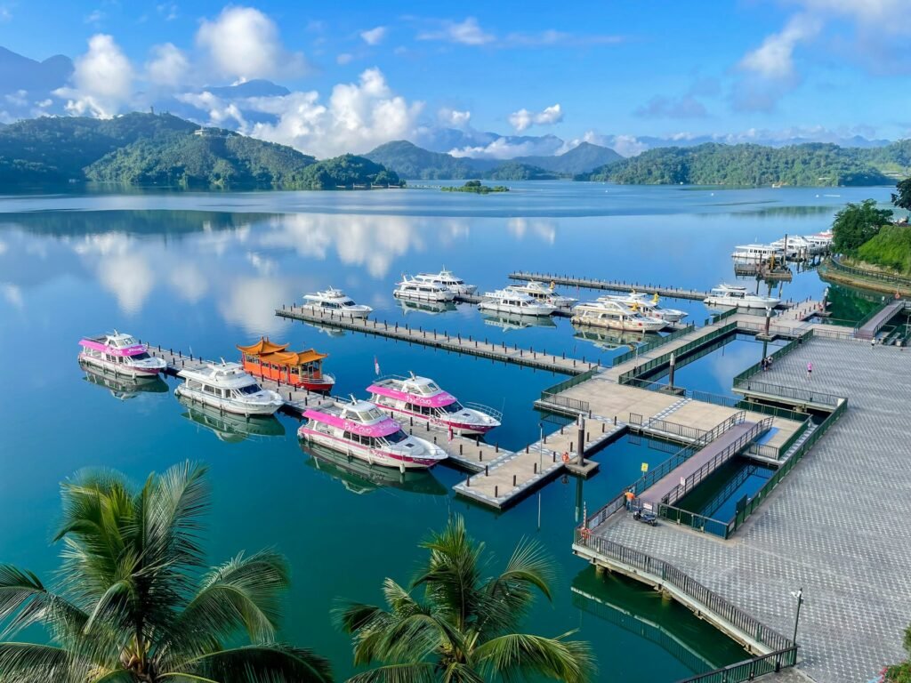 Tour boats, including one with a traditional pagoda roof, docked at a pier on the beautiful Sun Moon Lake in Taiwan, with mountains in the background.