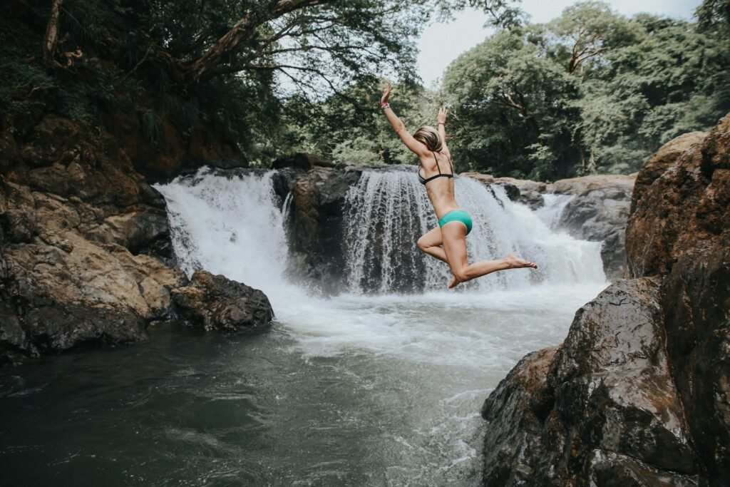 A woman in mid-air, cliff jumping into a natural pool at the bottom of a waterfall in a lush Costa Rican jungle.